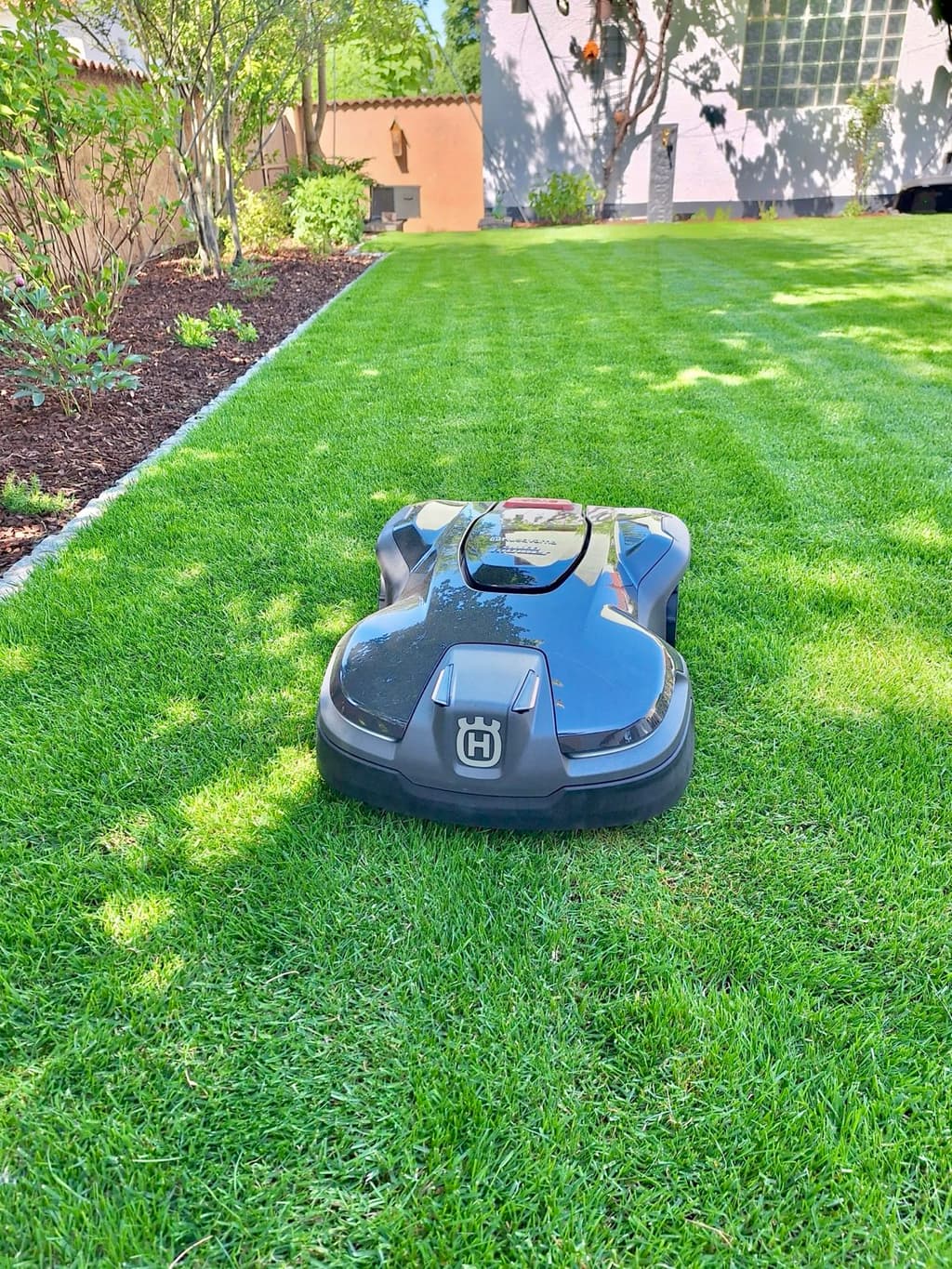 Mähroboter auf frisch gemähtem Rasen, daneben ein von Randsteinen eingefasstes Mulchbeet